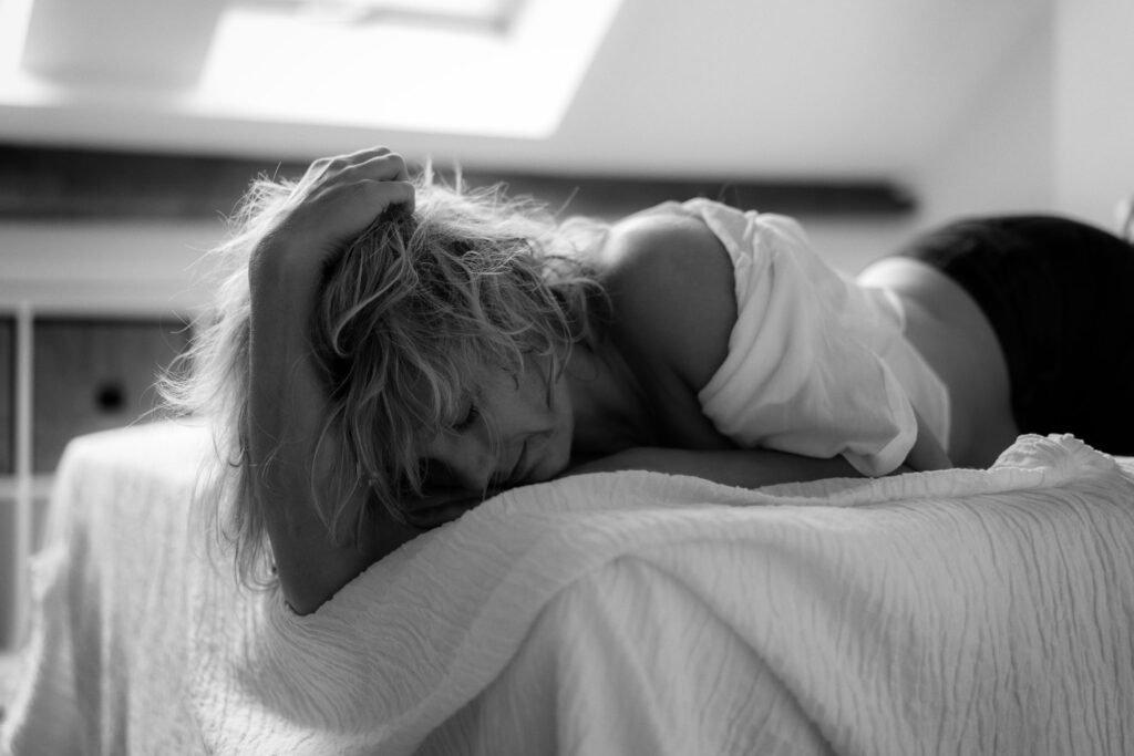 Girl wearing a black jeans and white shirt laying on her stomach on the bed with her head resting in her arm.